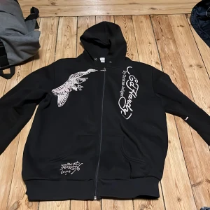 Svart hoodie från Ed Hardy - Säljer en svart hoodie från Ed Hardy med dragkedja och stora tryck både fram och bak. Jätte fint skick förutom en liten fläck. Pruta om du vill men inga skambud tack! 
