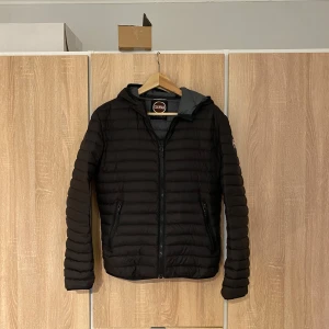 Svart pufferjacka från Colmar - Säljer en stilren svart pufferjacka från Colmar. Jackan har en dragkedja framtill och är långärmad med en huva. Perfekt för kyligare dagar och ger en modern look. Passar bra till både casual och mer uppklädda tillfällen.