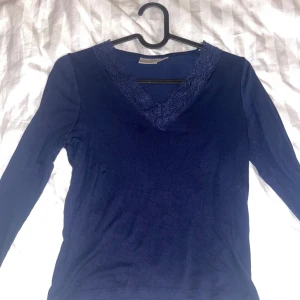 Mörkblå tröja med spetsdetaljer - Säljer en mörkblå tröja med v-ringning och spetsdetaljer runt halsen från Gina Young. Knappt använd så som ny, strl 146/150 och passar mig som har xs-s