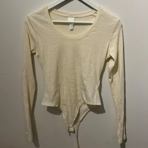 Cream vit långärmad bodysuit från H&M - Säljer en stilren cream vit långärmad string body från H&M. Den har en rund halsringning och är tillverkad i ett mjukt material som ger en bekväm passform. 