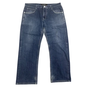 Blå jeans från Raw Blue - Snygga blå jeans från Raw Blue med unika broderade detaljer på bakfickorna. De är i perfekt skick och har aldrig blivit använda. Riktigt unik design på byxornas knappar.