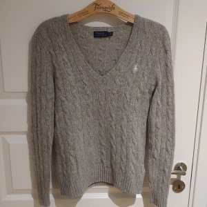 Kabelstickad kashmir/merinotröja från Ralph Lauren - Säljer denna ljuvliga kabelstickade tröjan i 10% kashmir, 90% merinoull. Hur mjuk och skön som helst! Sticks inte alls. Nyansen syns bäst på bild 2-4, ljusare än på första bilden. Stl S, funkar nog även för en XS, se mått. Sparsamt använd så i superskick, ej nopprig, inga defekter. Liknande säljs på rea för 2376 på Zalando, så detta är ett riktigt bra pris! Mått: Armhåla till armhåla 43cm, bredd längst ner 39cm, längd från mitt på axeln 59cm. 