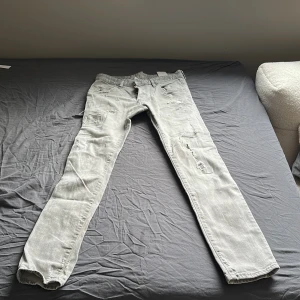 Grå jeans från DSQUARED2 - Snygga grå jeans från DSQUARED2 med slitna detaljer och knappgylf. Perfekta för en trendig look. Tillverkade i Italien med högkvalitativt material.
