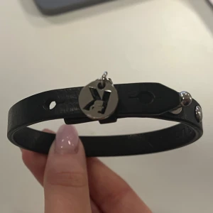 Svart armband med silverdetalj -  svart armband i skinn med en rund silverdetalj som har en ingraverad design. Armbandet har justerbara hål för perfekt passform och en stilren look. Kill armband, fin alla hjärtans dag present 