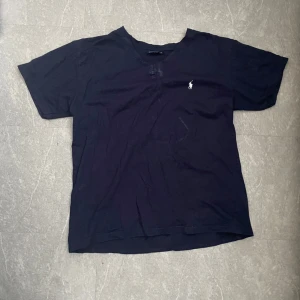 Marinblå  t-shirt från Polo - Säljer en klassisk marinblå t-shirt från Polo i storlek L. Den är tillverkad av 100% bomull och har en liten broderad logga på bröstet. Perfekt för en stilren och avslappnad look.