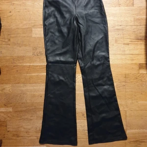 Svarta skinnbyxor från Gina Tricot - Snygga svarta skinnbyxor från Gina Tricot med dragkedja i sidan. Byxorna har en bootcut-stil som ger en trendig look. Perfekta för att höja din outfit med en edgy touch.