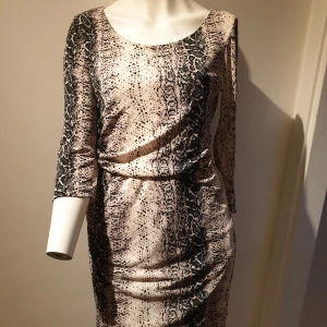 Mönstrad klänning med trekvartsärm - Snygg klänning med ett unikt mönster i svart och beige. Den har trekvartsärmar och en figurnära passform som framhäver silhuetten. Perfekt för en stilfull look.❗små tecken på slitage på framsidan, se bild 3, därav priset 