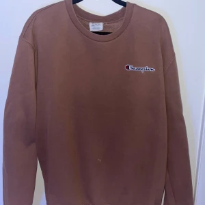 Champion sweatshirt brun - Säljer en brun sweatshirt från Champion med deras ikoniska logga på bröstet. Tröjan har en klassisk rund hals och långa ärmar, perfekt för en avslappnad stil. Passar bra till både jeans och joggers. 