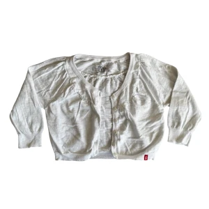 Söt vit kofta - Säljer en söt vit kofta med knappar framtill. Koftan har trekvartsärmar och en liten röd etikett vid nederkanten. Perfekt för lager-på-lager-stil.