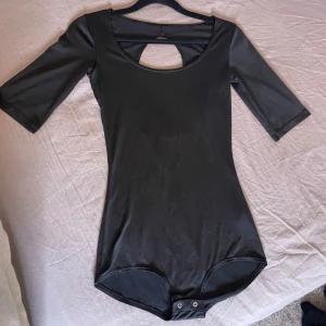 Svart body med öppen rygg - Snygg svart body med trekvartsärm och en stilren öppen ryggdetalj. Perfekt för en elegant look. Materialet är mjukt och stretchigt för en bekväm passform.