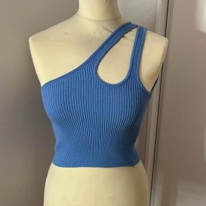 Blå oneshoulder ribbad topp - Snygg blå oneshoulder topp i ribbat material. Perfekt för sommardagar eller en utekväll. Den har en tight passform som framhäver figuren. Ett måste i garderoben för den som gillar att sticka ut!