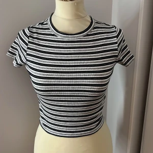 Randig ribbad topp - Säljer en superfin randig topp i svart och vit. Den är ribbad och har en croppad passform som är perfekt för sommaren. Toppen har korta ärmar och en rund halsringning. Perfekt för en avslappnad dag eller en somrig utflykt!
