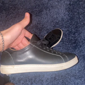 Svarta sneakers från selected homme - Säljer ett par stilrena svarta sneakers i skinn med vit sula. De har klassisk snörning och är i mycket bra skick. Perfekta för både vardag och fest. Passar till det mesta i garderoben! De är från selected homme. PRIS GÅR ATT DISKUTERA