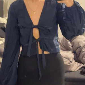 Mörkblå blus med knytning - Snygg mörkblå blus med knytning framtill. Den har långa ärmar och en v-ringad design som ger en elegant look. Perfekt för både vardag och festliga tillfällen. Passar bra med jeans eller kjol för en chic outfit. Den är aldrig använd endast testad och jag köpte den för 300kr så jag säljer dne för 200kr💗 då den är så ny. 