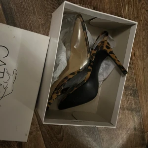 Leopardmönstrade klackskor från EGO - Snygga klackskor från EGO med leopardmönster och transparenta detaljer. De har en spetsig tå och hög klack, perfekt för en utekväll eller fest. Skorna är i mycket bra skick och ger en trendig look. 