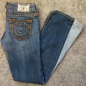 Blå jeans från True Religion - Säljer ett par snygga blå flarejeans från True Religion 🪭 De har en cool design med orange kontrastsömmar och klassiska bakfickor med broderad logga. Jeansen är i bra skick och perfekta för vardagsbruk eller en avslappnad utekväll. Finns ett par lösa sömmar men det är inget man tänker på. ⭐️ Säljer pga de är för små för mig. Midja: 35 cm 