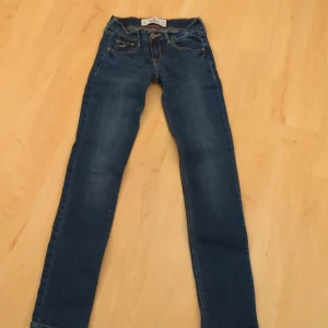 Blå jeans från Hollister - Säljer ett par snygga blå jeans från Hollister. De är i bra skick och har en klassisk femficksdesign med snygga sömmar på bakfickorna. Perfekta för vardagsbruk och kan enkelt matchas med olika outfits. Passformen är tight och de är tillverkade i ett bekvämt denimtyg. Kan inte visas på då de är försmå.