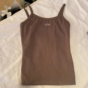 Brun linnetopp från DOM - Säljer en snygg brun linnetopp från DOM. Den är ärmlös med smala axelband och har en enkel design som passar perfekt till sommaren. Toppen är i bra skick och är superbekväm att ha på sig!