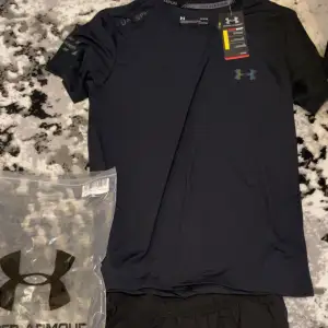 Säljer en svart t-shirt & shorts från Under Armour i nytt skick. Perfekt för träning med sin lätta och bekväma passform. T-shirten är kortärmad och har den klassiska loggan på bröstet. Kommer med originalförpackning. Helt ny