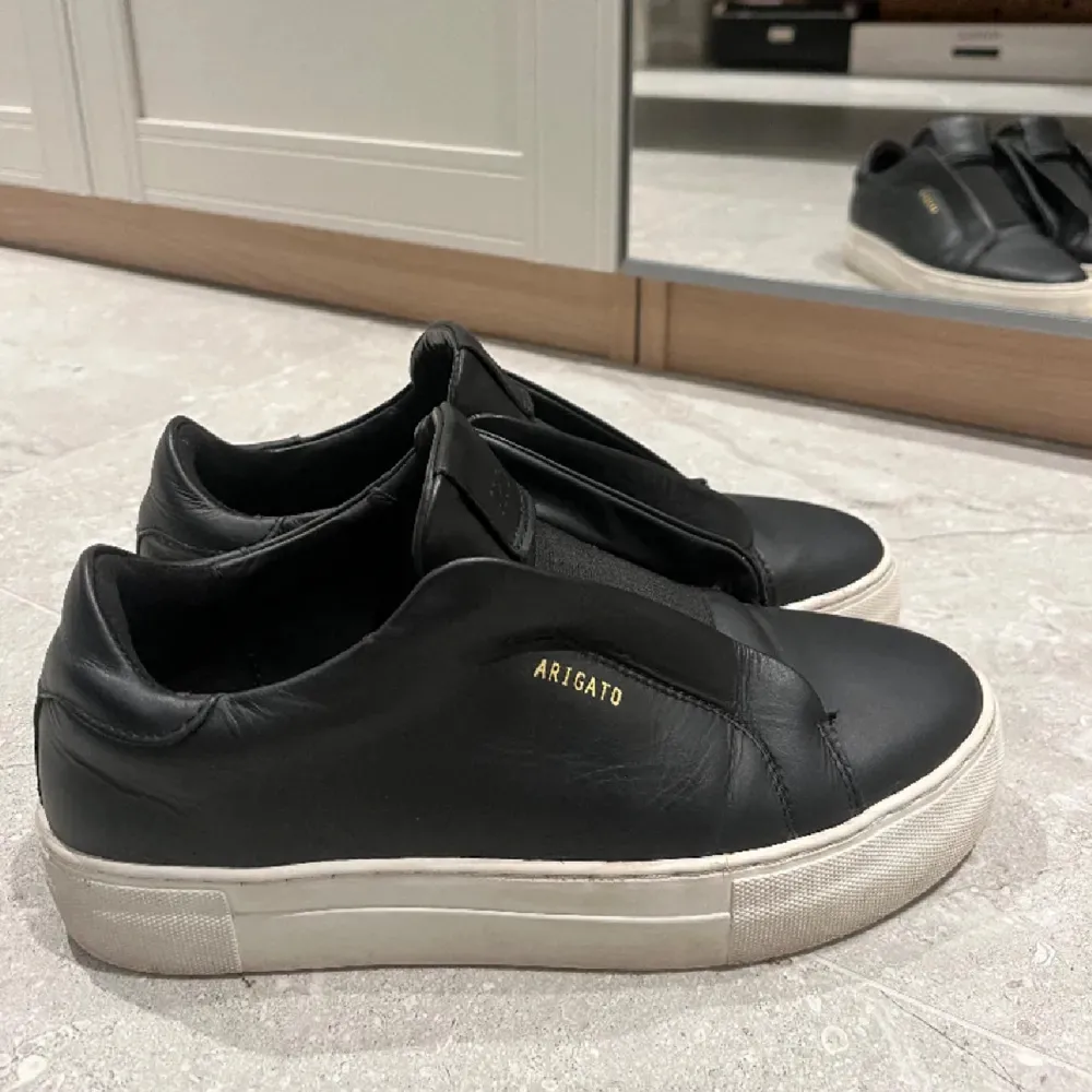 Säljer ett par stilrena svarta sneakers från Axel Arigato i skinn. Perfekta för en casual look eller att klä upp med något snyggt. Använda men i bra skick. Passar till det mesta och är superbekväma!. Skor.