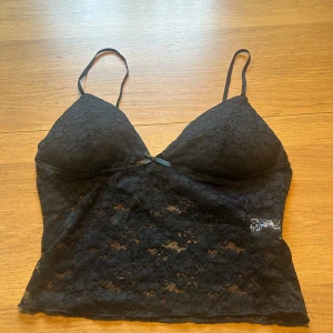 Svart spetslinne - Snyggt svart spetslinne med tunna axelband. Perfekt för en utekväll eller fest. Det är i bra skick och har en elegant design med spetsdetaljer som ger en romantisk känsla. Passar bra till både jeans och kjol.