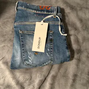 Säljer ett par snygga blå jeans från Dondup i storlek 30. De har en cool slitningseffekt och klassisk femficksdesign. Perfekta för en avslappnad stil, oavsett om det är vardag eller fest. Passar bra till både sneakers och boots! Bara att hör av sig till oss vid frågor och funderingar.