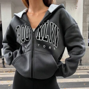 Grå hoodie med Brooklyn-tryck - Säljer en snygg grå hoodie med stort Brooklyn-tryck på framsidan. Den har en dragkedja och en mysig huva med vit insida. Perfekt för en casual look eller när du vill hålla dig varm under kyliga dagar. Passar bra till jeans eller leggings!