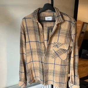 Beige rutig skjorta från Woodbird - Säljer en snygg beige rutig skjorta från Woodbird. Skjortan har långa ärmar och en klassisk krage med knappar framtill. Perfekt för höst och vår, och funkar både till vardags och fest. Den är i mycket bra skick och har en skön, avslappnad passform.