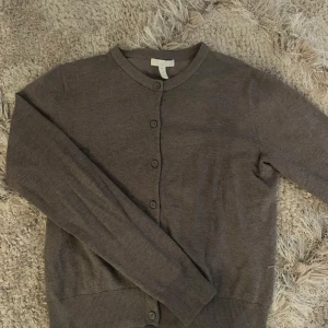 Brun kofta från H&M - Säljer en stilren brun kofta från H&M i storlek S. Den är i bra skick och perfekt för både höst och vår. Koftan har långa ärmar och knappar framtill, vilket gör den lätt att matcha med olika outfits. Supermysig och enkel att bära till vardags!