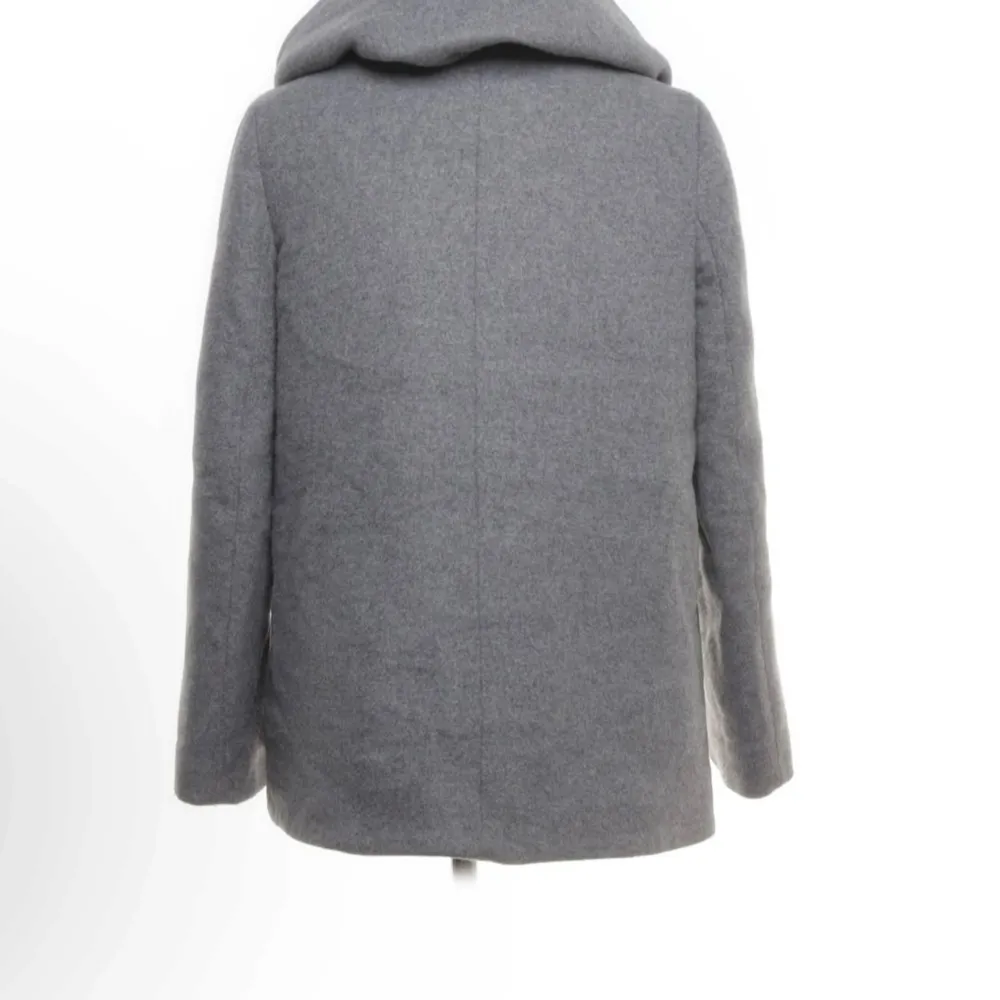 Säljer en stilren grå kappa med stor huva och knappar framtill. Perfekt för höst och vinter, den håller dig varm och snygg. Kappan har en normal passform och är i mycket bra skick. Den är långärmad och har en enkel men elegant design 💗. Takit.
