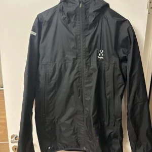 Svart vindjacka från Haglöfs - Säljer en svart vindjacka från Haglöfs L.I.M Series i storlek M. Jackan har en dragkedja framtill och är perfekt för utomhusaktiviteter. Den är lätt och smidig, vilket gör den idealisk för vår och höst. Perfekt för dig som gillar att vara aktiv och behöver en pålitlig jacka!