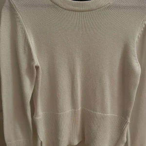 Beige stickad tröja - Säljer en superfin vit stickad tröja i bra skick. Den har långa ärmar och ribbade detaljer vid ärmslut och nederkant, samt slits. 