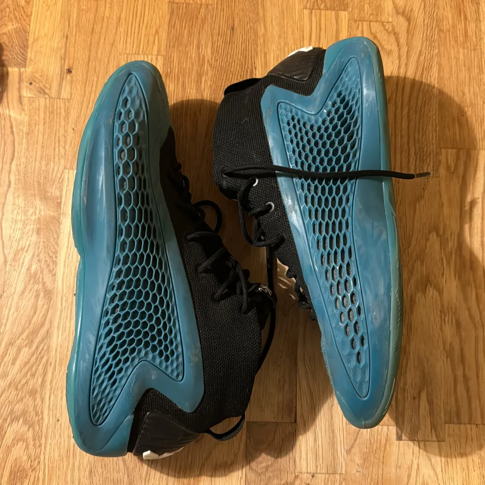 Säljer ett par grymma basketskor (AE1s) från Adidas i svart och blått. De har en unik design med blå sula och detaljer, samt svart ovandel. Perfekta för både basket men också vanlig träning i gymmet. Skorna har bra snörning och är i okej skick. Stor logga på hälen ger en extra touch. Pris kan självklart diskuteras!. Skor.