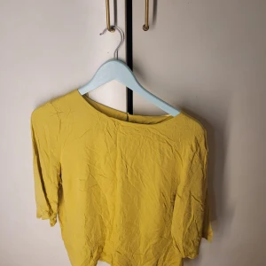 Gul blus från KappAhl - Säljer en solgul blus från KappAhl i storlek 44. Blusen har trekvartsärmar och en enkel design med en liten knappdetalj i nacken. Perfekt för vår och sommar! 🌼