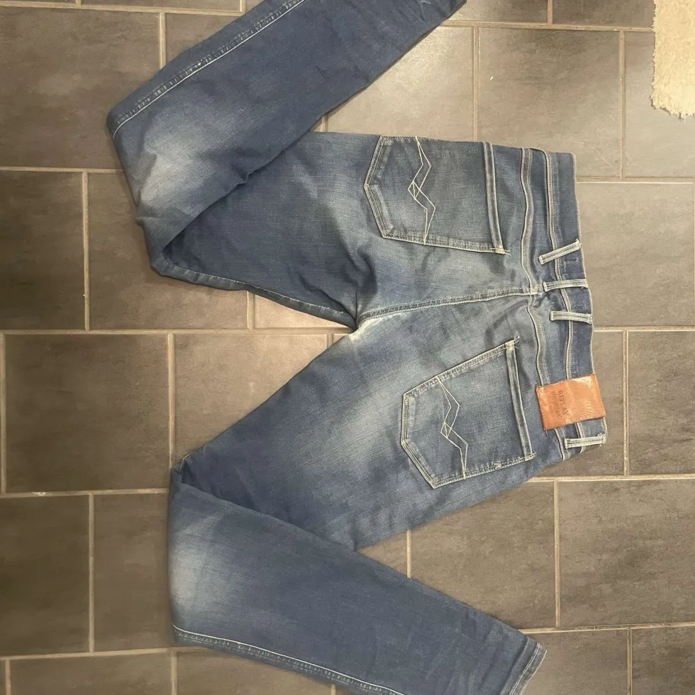 Säljer ett par snygga blå jeans från Replay i modellen Anbass. De har en slim passform och är i bra skick med en cool tvättad look.  Har däremot lite slitningar i skrevet. Perfekta för både vardag och fest! 🕺. Jeans & Byxor.