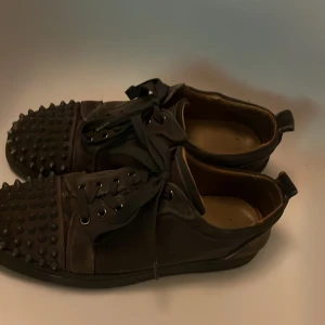 Loubs - Säljer ett par coola svarta sneakers med nitar på tån och röd sula. De har snörning och är i bra skick. Perfekta för att ge din outfit en lite coolare look