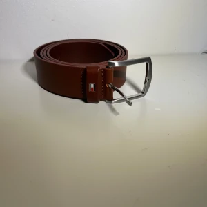 Tommy Hilfiger bälte - Brunt bälte från Tommy Hilfiger i läder. Storlek 115