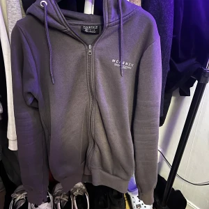 Grå hoodie från McKenzie - Säljer en grå hoodie från McKenzie i storlek XS. Den har en dragkedja framtill och en mysig huva med snören. Perfekt för kyliga dagar eller som ett extra lager. Använd men i bra skick!