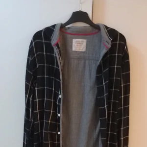 Svart och vit rutig skjorta - Säljer en stilren svart och vit rutig skjorta med långa ärmar. Skjortan har knappar hela vägen ner och en klassisk krage. Perfekt för både vardag och festliga tillfällen. Passar bra till jeans eller chinos för en avslappnad look.