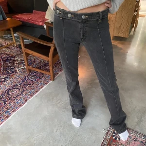 Svarta jeans med knappar - Säljer ett par snygga svarta jeans i bra skick. De har en lågmidjad passform med knappar framtill och en bootcut-stil. Perfekta för både vardag och fest! 🖤LÅNAD BILD FRÅN HON JAG KÖPTE AV