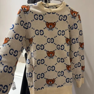 Beige stickad tröja med björnmönster - Säljer en superfin beige stickad tröja från Gucci med ett gulligt björnmönster och blå detaljer. Perfekt för höst och vinter! Tröjan har långa ärmar och är i mycket bra skick. Passar perfekt för att hålla sig varm och stilren. 🐻💙storlek M