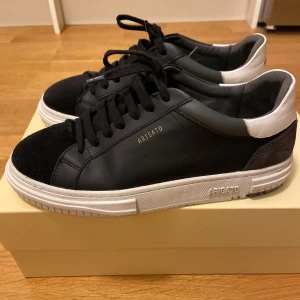 Svarta sneakers från Axel Arigato - Säljer ett par snygga svarta sneakers från Axel Arigato i mycket bra skick. Skorna har en stilren design med svart skinn och mocka, samt vita detaljer på hälen. Perfekta för både vardag och fest i storlek 40