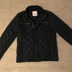 Navy quiltad jacka från Lindbergh - Tja, säljer snygg navy quiltad jacka från Lindbergh i storlek S. Jackan har dragkedja och knappar framtill samt två praktiska bröstfickor med dragkedja. Perfekt för höst och vinter sesongen, med en stilren look som passar både till vardags och fest. Original pris: 1499. Vårt pris: 649. 