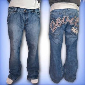 Blå jeans med broderad text - Säljer ett par coola blå jeans med en unik broderad text på baksidan. Dem är baggy. Midjemått tvärs över: 46cm innerben: 82cm (jeansen har ett snöre inne i midjan och funkar som ett bälte)