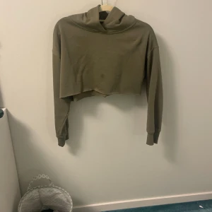 Olivgrön croppad hoodie - Säljer en olivgrön croppad hoodie i bra skick. Den har en avslappnad passform med långa ärmar och en mysig huva. Perfekt för en chill dag eller att slänga på sig efter träningen. Passar bra till både jeans och leggings!    Den är avklippta med repar inte upp sig, nästan aldrig använd