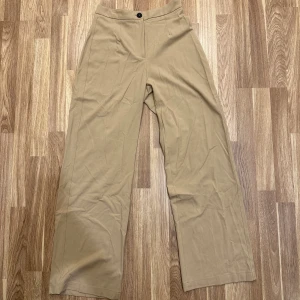 Beige kostymbyxor - Stilrena beige kostymbyxor från Bershka i storlek 38. De är högmidjade med en knapp fram och baktill för fickan! Helt oanvända!