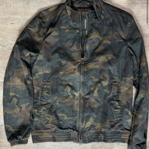 Woolrich windbreaker - Säljer en snygg camouflage windbreaker från Woolrich i storlek M. Jackan har en dragkedja framtill och är perfekt för höst och vår.  Perfekt för dig som vill ha en stilren jacka! Jackan är i bra skick och säljer den till ett bra pris. Pris kan diskuteras! 