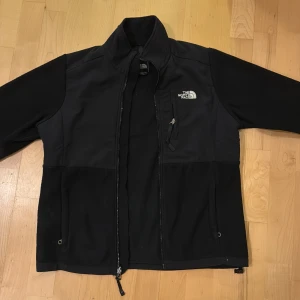 Svart fleecejacka från The North Face - Säljer en svart fleecejacka från The North Face i bra skick. Jackan har en dragkedja framtill och en bröstficka med dragkedja. Perfekt för kyliga höst- och vårdagar. Den är långärmad och har en normal passform. Supermysig och praktisk för utomhusaktiviteter!