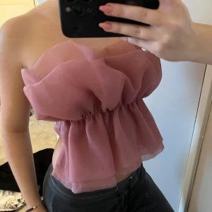 Rosa axelbandslös topp från Zara - Säljer en superfin rosa axelbandslös topp från Zara. Den har en fluffig och volangig design som ger en romantisk känsla. Perfekt för sommarens fester eller en utekväll. Toppen är i mycket bra skick och redo för nya äventyr!