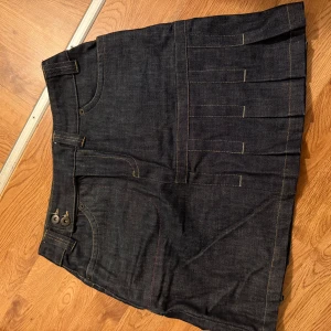 Jeanskjol från Cheyenne - Säljer en cool jeanskjol från Cheyenne i storlek 38. Kjolen har en klassisk mörkblå denimfärg med snygga veckdetaljer och praktiska fickor både fram och bak. Perfekt för en avslappnad vardagslook eller en utekväll. Passar bra till både sneakers och boots!